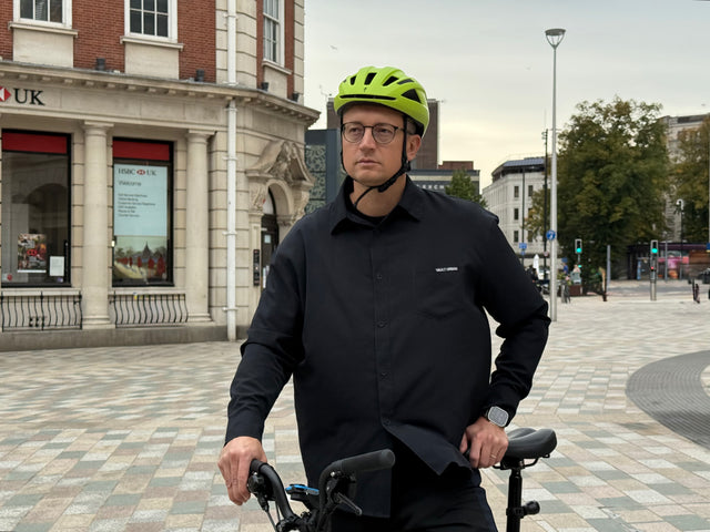 Man wearing a black Vault Urban sustainable wrinkle-free shirt, standing with a bicycle in an urban city setting