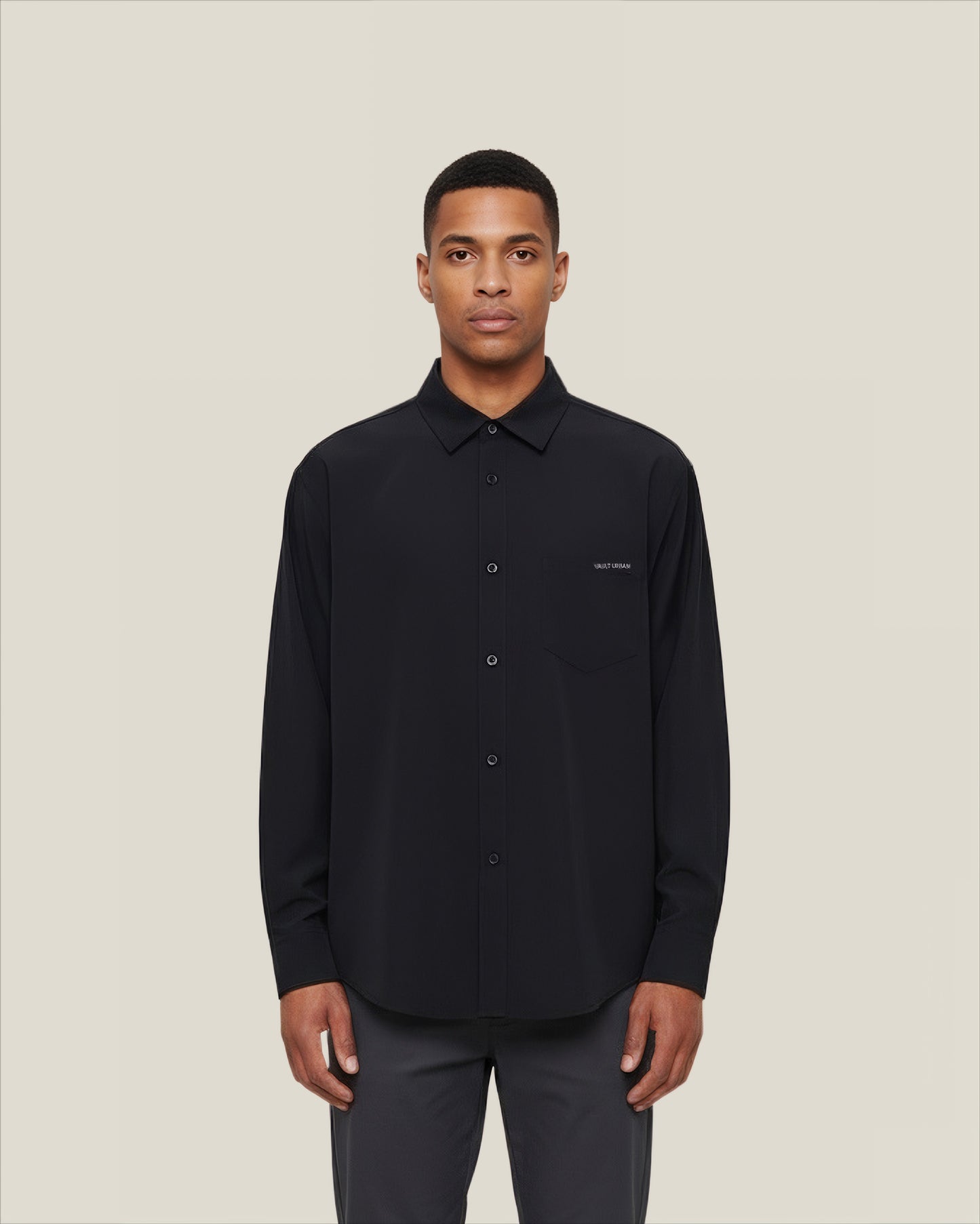 Man wearing a black shirt with a small logo on a beige background