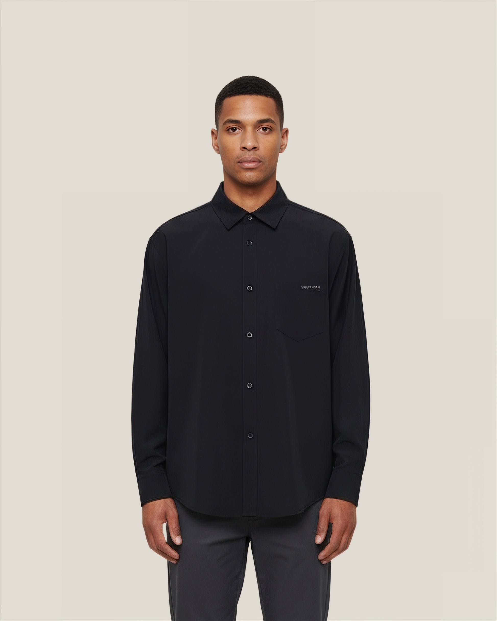 Man wearing a black shirt with a small logo on a beige background